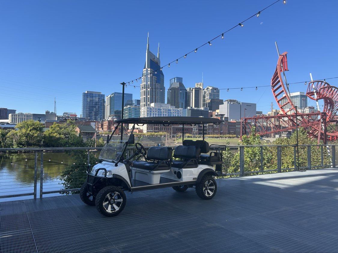 White golf cart on the Nashville riverfront with the downtown skyline behind it